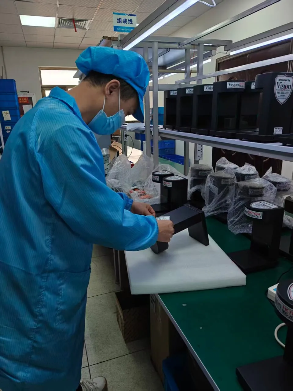 A technician labelling a Vision MCD-900-1 detector on the assembly line, with finished units on the shelf behind