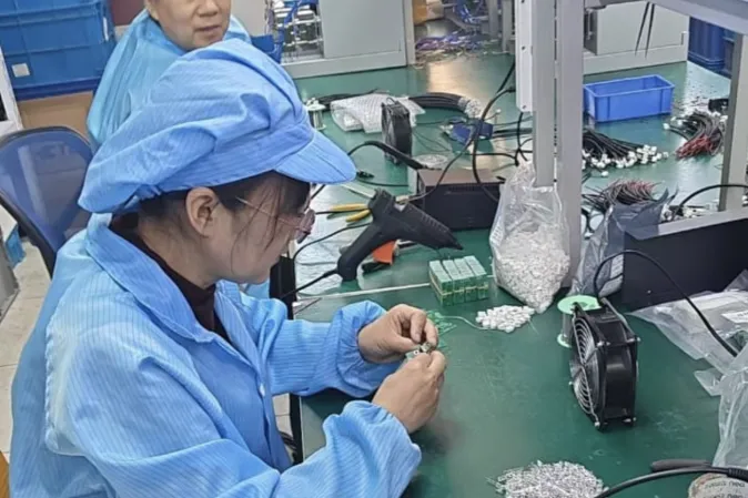 A technician hand-wiring internal components at an assembly bench